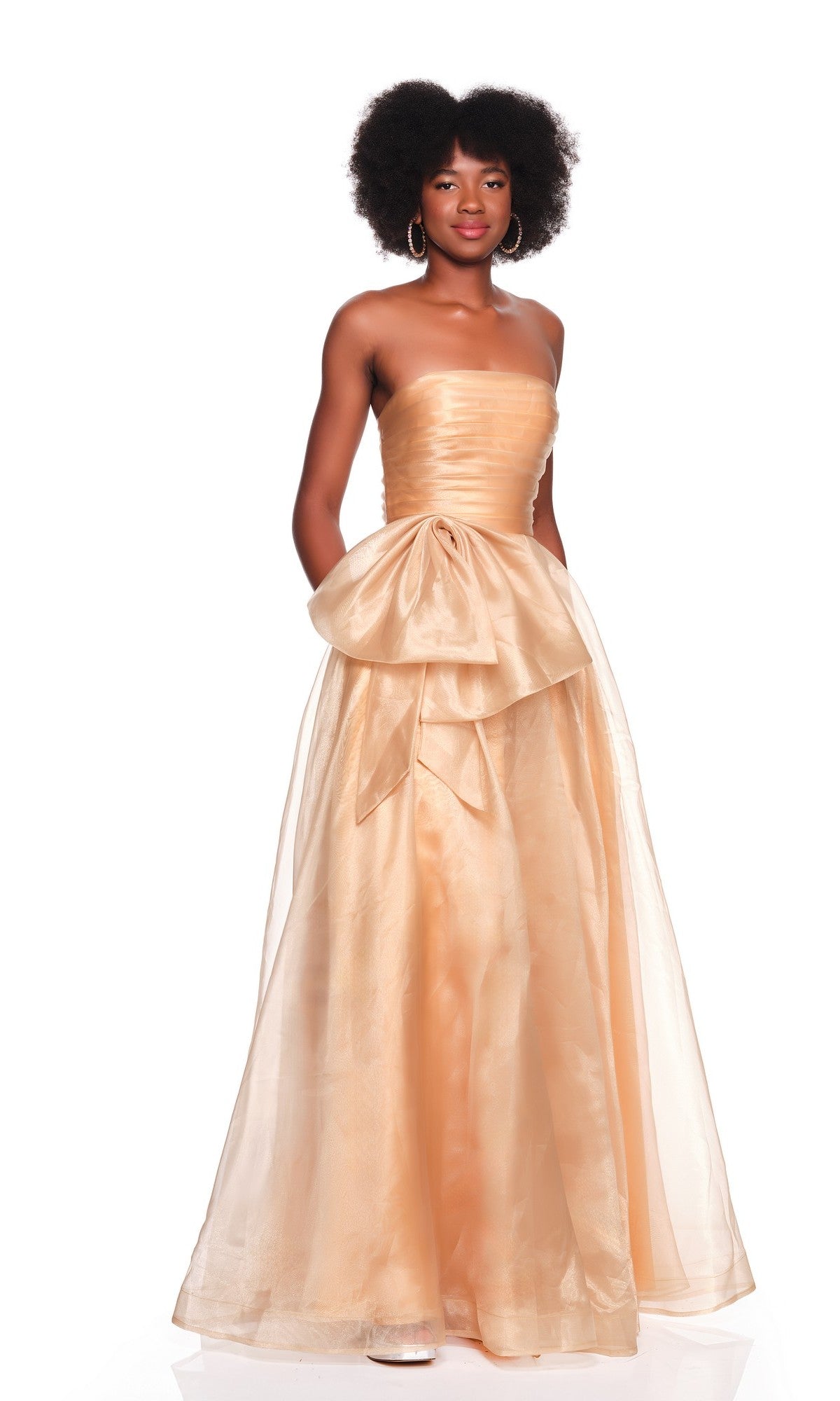 A woman poses against a white background wearing the peach Long Prom Dress: Dave and Johnny 12629, featuring a strapless ruched fitted bodice, full sheer tulle a-line skirt, and an elegant large bow.